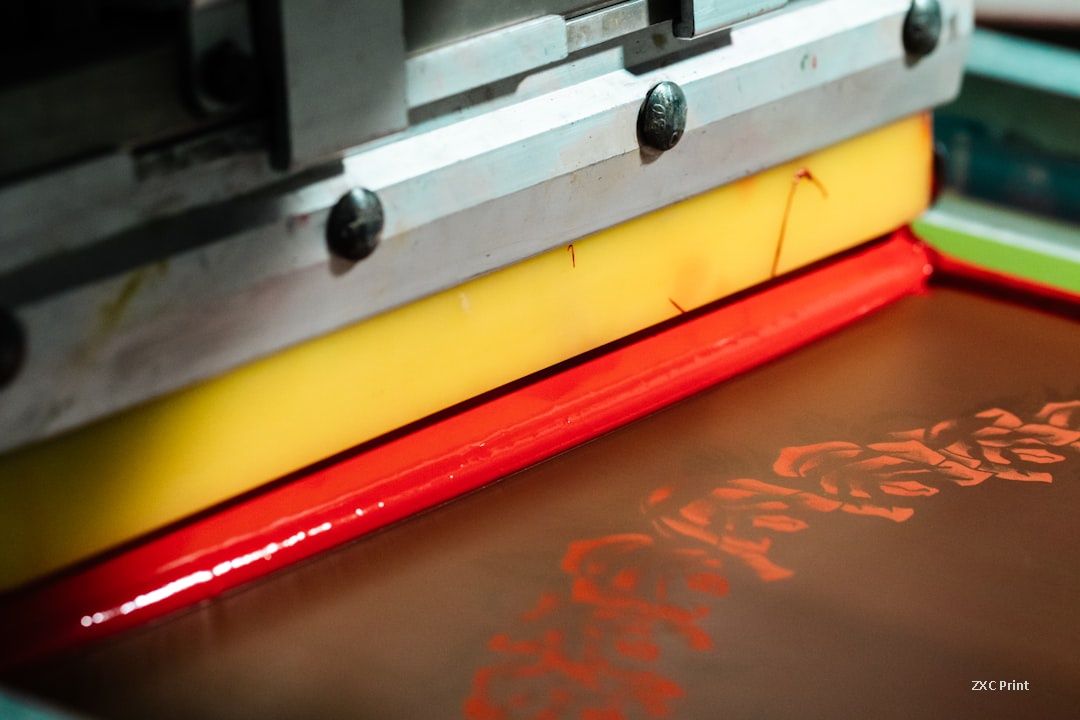 Close-up of a screen printing squeegee pushing red ink through a dark mesh screen