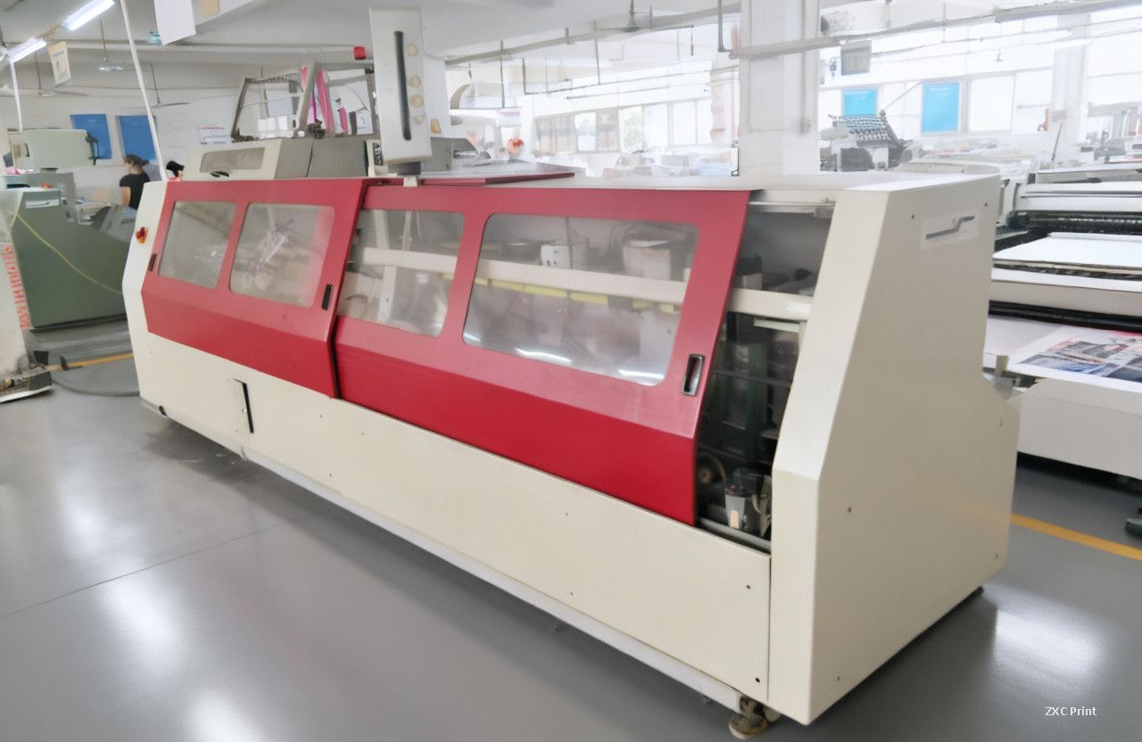 Book binding machine with red sliding doors standing on a factory floor