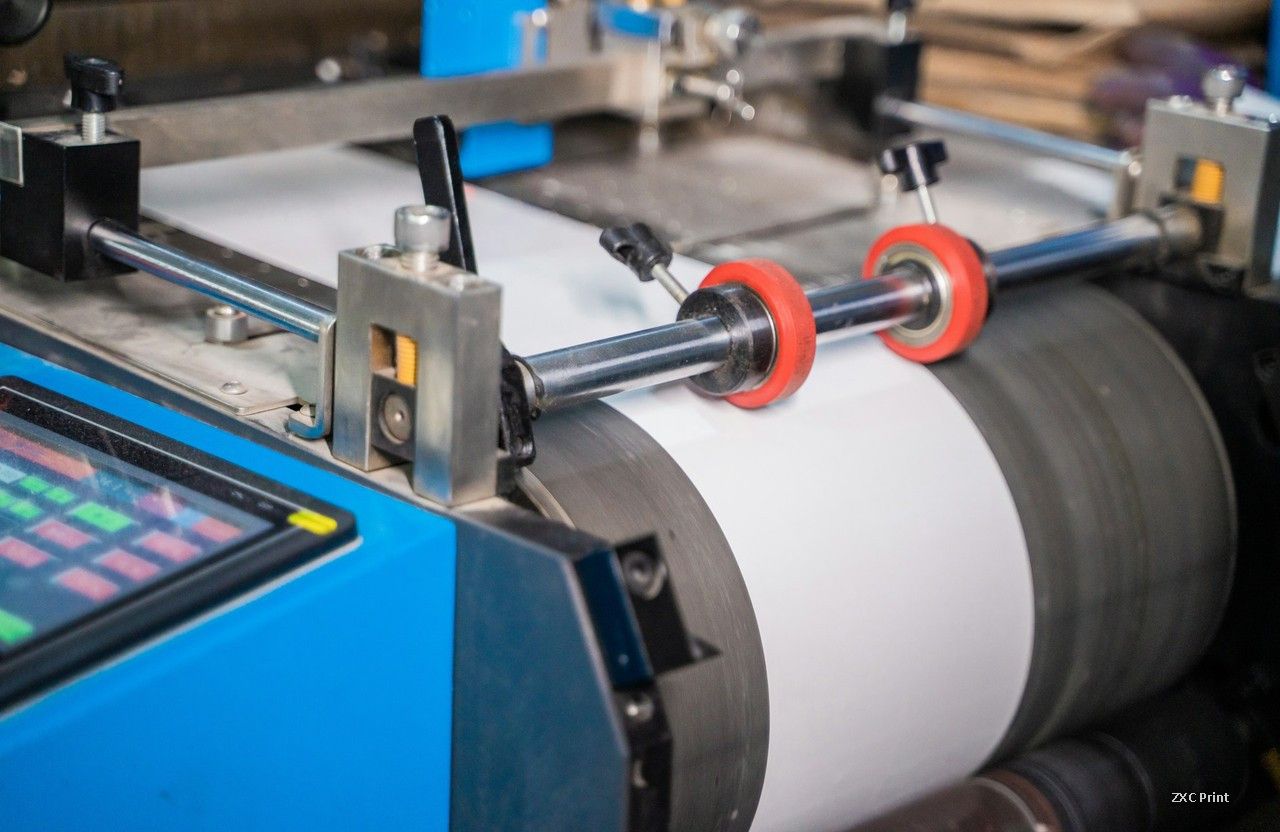 Web fed flexographic press with a white substrate running over a large impression cylinder and red nip rollers